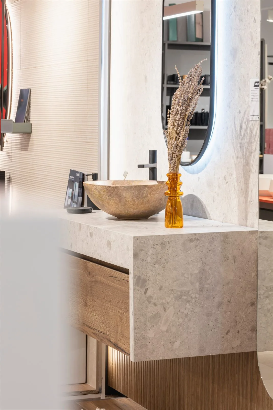 Encimera de piedra con lavabo de mármol, grifería negra y jarrón ámbar con flores secas