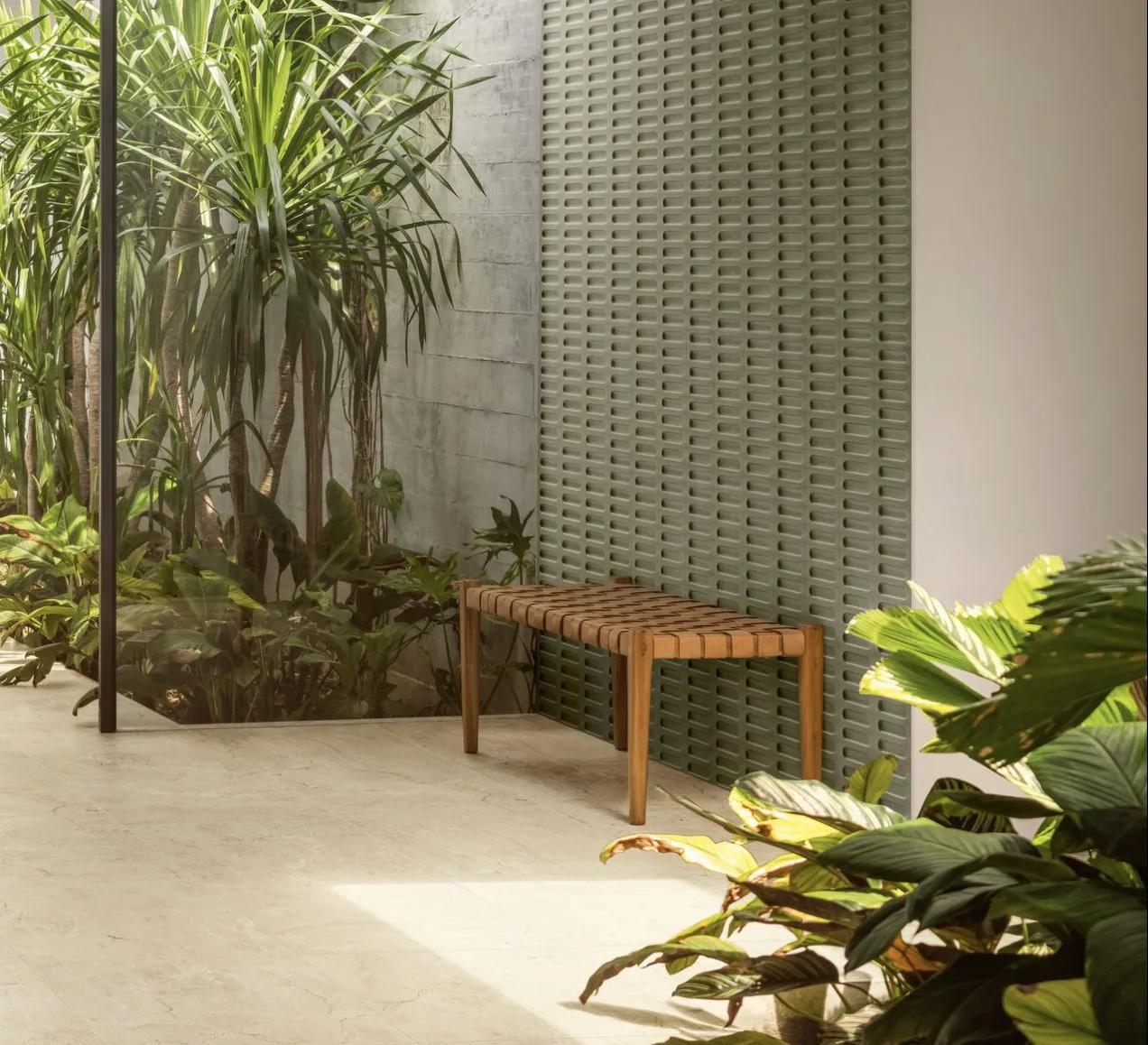 Patio interior con celosía de piezas cerámicas verdes, banco de madera y vegetación tropical